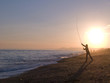 Silhouette of man casting with fishing rod into ocean at sunset
