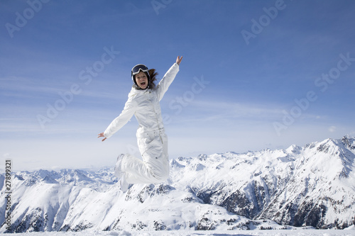 Photo: Young woman in ski gear jumping in midair in the mountains Young woman in ski gear jumping in midair in the mountains