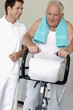 A senior man on an exercise bike, physiotherapist by his side
