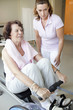 A senior woman working out on a rowing machine, fitness instructor at her side