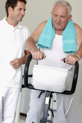 Photo: A senior man on an exercise bike, physiotherapist by his side A senior man on an exercise bike, physiotherapist by his side