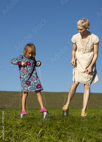 Photo: A mother and daughter playing outside on tin can stilts A mother and daughter playing outside on tin can stilts