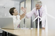 Photo: Two businessmen sitting in an office with model wind turbines celebrating success Two businessmen sitting in an office with model wind turbines celebrating success