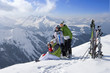 Family sitting in snow on mountain top with skis