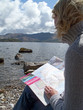 Woman looking at map and sitting rocky shore of lake