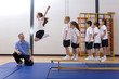 Gym teacher watching school girl jump off bench in school gymnasium