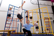 Gym teacher watching school boy jumping off climbing equipment