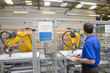 Worker watching robotic arm working on assembly line in factory