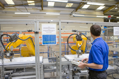 Photo: Worker watching robotic arm working on assembly line in factory Worker watching robotic arm working on assembly line in factory