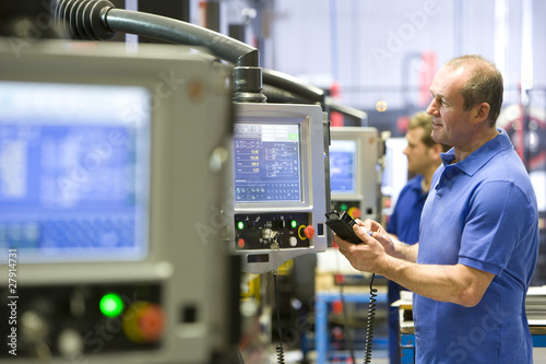 Photo: Worker operating computer controlled machinery in factory that manufactures aluminium light fittings Worker operating computer controlled machinery in factory that manufactures aluminium light fittings
