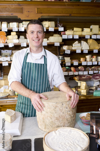 Photo: Salesman standing at counter with cheese in cheese shop Salesman standing at counter with cheese in cheese shop
