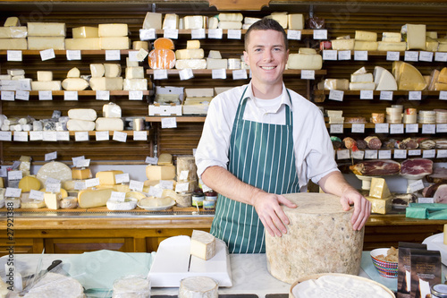 Photo: Salesman standing at counter with cheese in cheese shop Salesman standing at counter with cheese in cheese shop