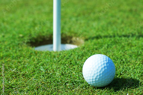 Photo: Golf ball on green grass in front of hole Golf ball on green grass in front of hole