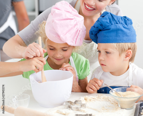 Photo: Two children and their mother stiring a preparation for cookies Two children and their mother stiring a preparation for cookies