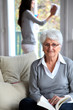Elderly woman reading book while housekeeper cleans windows Elderly woman reading book while housekeeper cleans windows