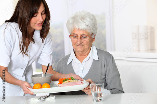 Photo: Beautiful nurse bringing meal tray to old woman at nursing home Beautiful nurse bringing meal tray to old woman at nursing home