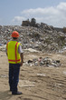 Worker watching digger moving waste at landfill site