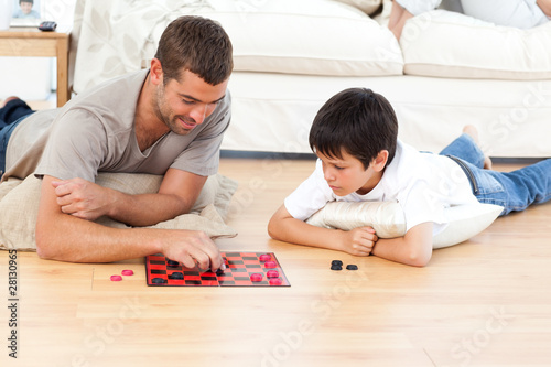 Photo: Handsome man playing checkers with his son lying on the floor Handsome man playing checkers with his son lying on the floor