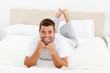 Handsome man laughing lying on his bed
