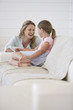 Mother crouching next to girl sitting on sofa