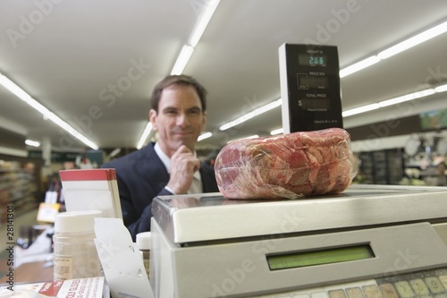 Photo: Mature man looks at selected meat on weighing machine Mature man looks at selected meat on weighing machine
