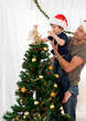 Cute son decorating the christmas tree with his father