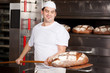 zufriedener bäcker holt brot aus dem ofen