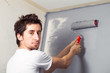 Young man paints a wall with a gray paint