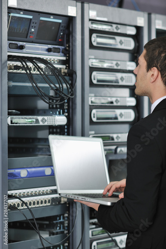 Foto: businessman with laptop in network server room businessman with laptop in network server room