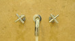 Metallic Faucet on yellow Ceramic wall with water drop