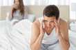 Photo: Man having a headache sitting on the bed with his girlfriend Man having a headache sitting on the bed with his girlfriend