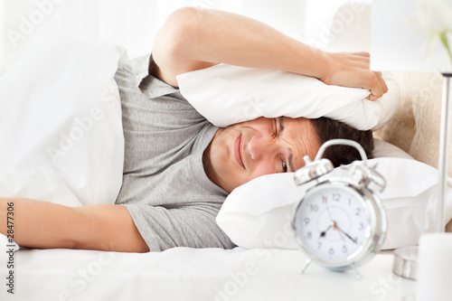 Photo: Stressed man looking at his alarm clock ringing Stressed man looking at his alarm clock ringing