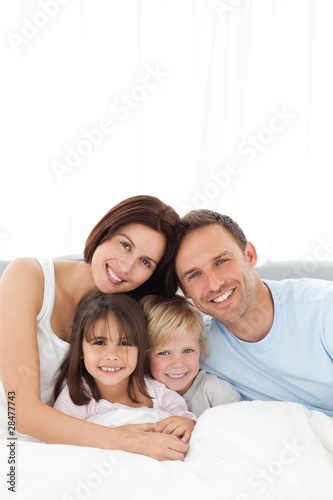 Photo: Portrait of a joyful family sitting on the bed Portrait of a joyful family sitting on the bed
