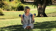 Old woman working her muscles with dumbbells sitting on the grass