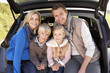 Young family pose together at rear of car