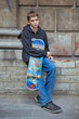 The teenager costs at a wall with a skateboard and has a rest.