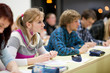pretty female college student sitting in a classroom full of stu