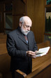 Standing Senior Caucasian Man Reading Hymnal In Church Pew