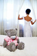 Foto: Bride near window and teddy bear on white bed Bride near window and teddy bear on white bed