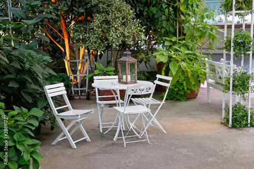 Photo: White table and chairs in beautiful garden. White table and chairs in beautiful garden.