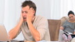 A desperate man on his laptop while his family is on the sofa