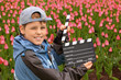 Boy with cinema clapper board standing on field with tulips