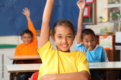 Photo: Three primary school children hands raised in class Three primary school children hands raised in class