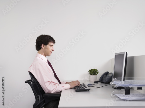 Photo: Male office worker using computer at desk in office Male office worker using computer at desk in office