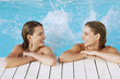 Two young women in pool at poolside splashing feet, front view