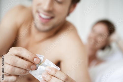 Foto: Couple in bed, man opening condom, close up of condom Couple in bed, man opening condom, close up of condom