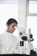 Female lab worker using microscope to examine petri dish