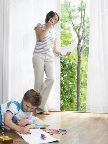 Photo: Mother using cell phone, young son drawing on floor Mother using cell phone, young son drawing on floor