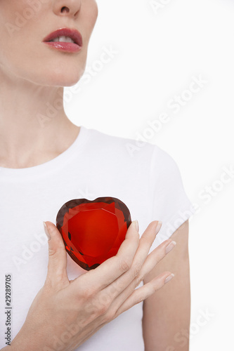 Photo: Woman holding heart-shaped jewel between finger and thumb Woman holding heart-shaped jewel between finger and thumb