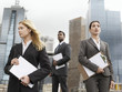 Three business people with clipboards outside office buildings